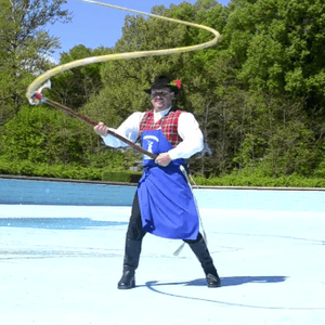 A person in a tartan vest and top-hat raises their whip dramatically into the air